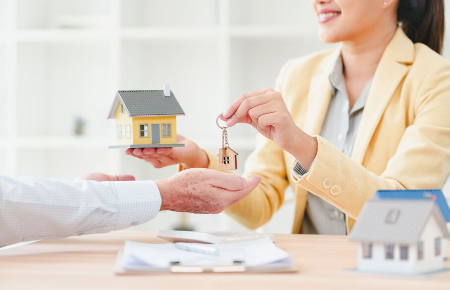 Young realtor handing house key to client with miniature house model 