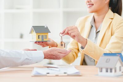 Young realtor handing house key to client with miniature house model 