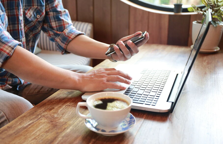 Person sat at the coffee table typing on their laptop whilst also on their phone