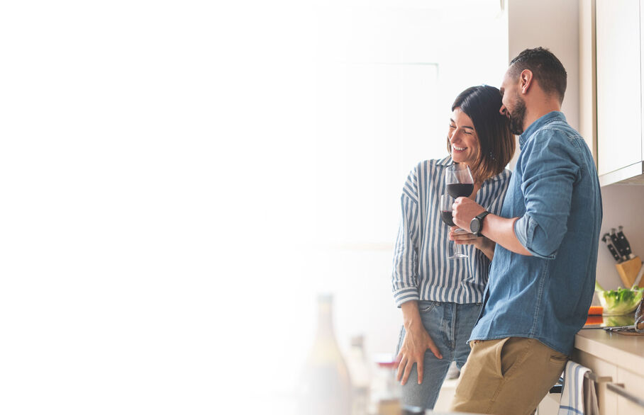 Couple leaning against kitchen tops with glasses of red wine