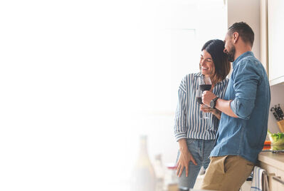 Couple leaning against kitchen tops with glasses of red wine
