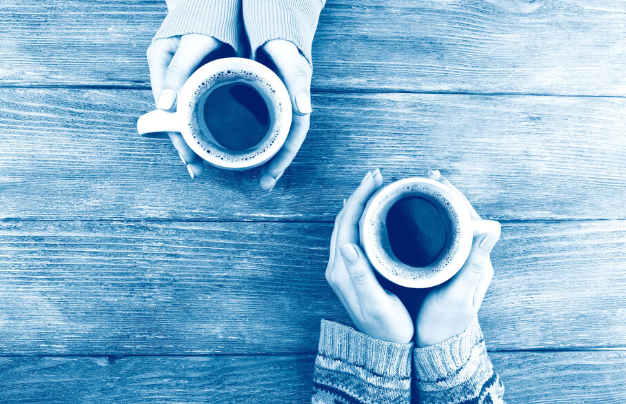 Two coffee cups being held across a table