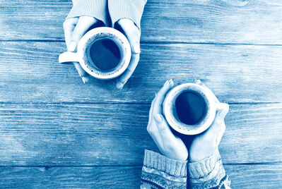 Two coffee cups being held across a table